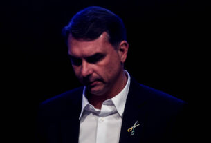 Flávio Bolsonaro adota broche de tesoura em pré-campanha e defende corte de gastos públicos