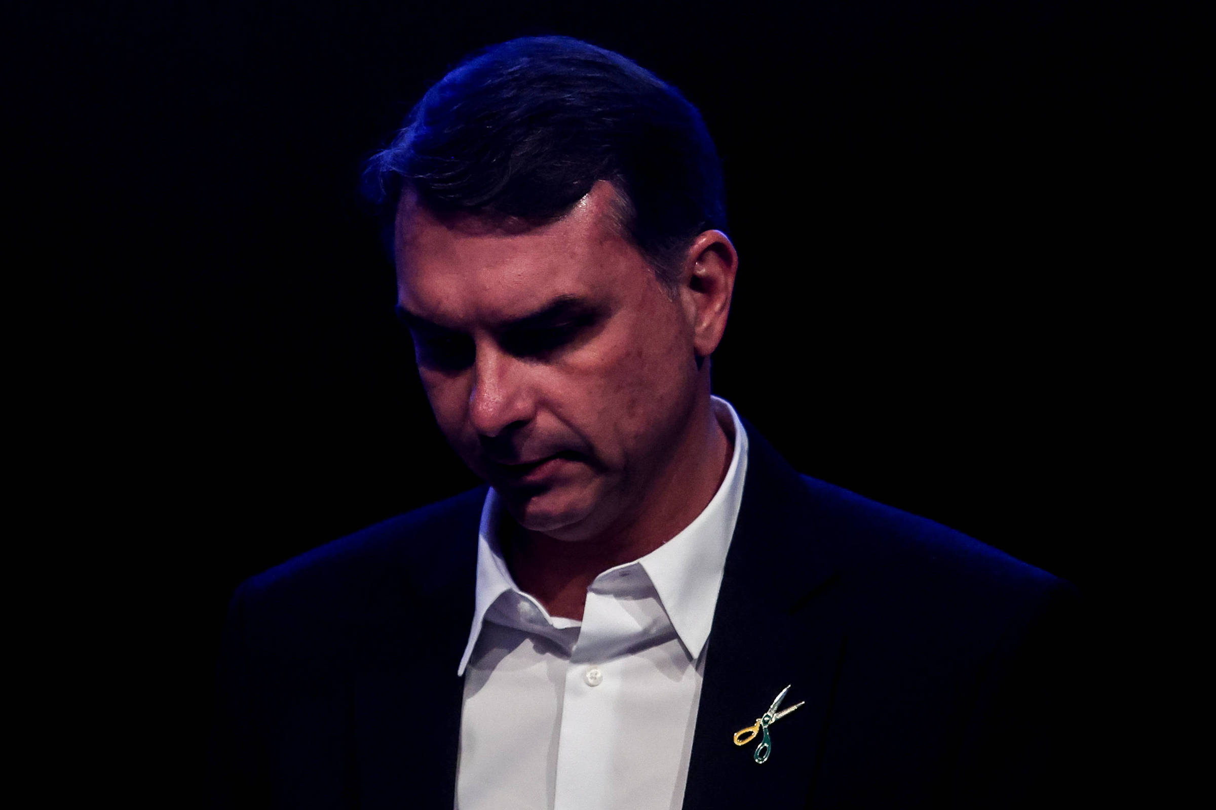 Flávio Bolsonaro adota broche de tesoura em pré-campanha e defende corte de gastos públicos